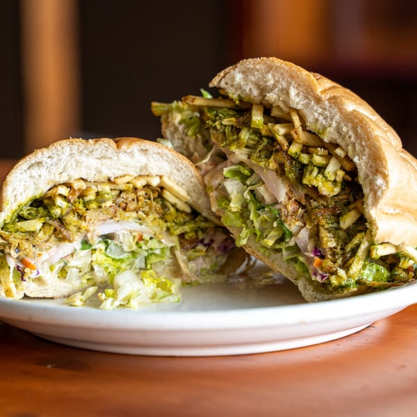 A Peruvian sandwich, cut in half, revealing chicken, green sauce, lettuce, and fries on a white plate.