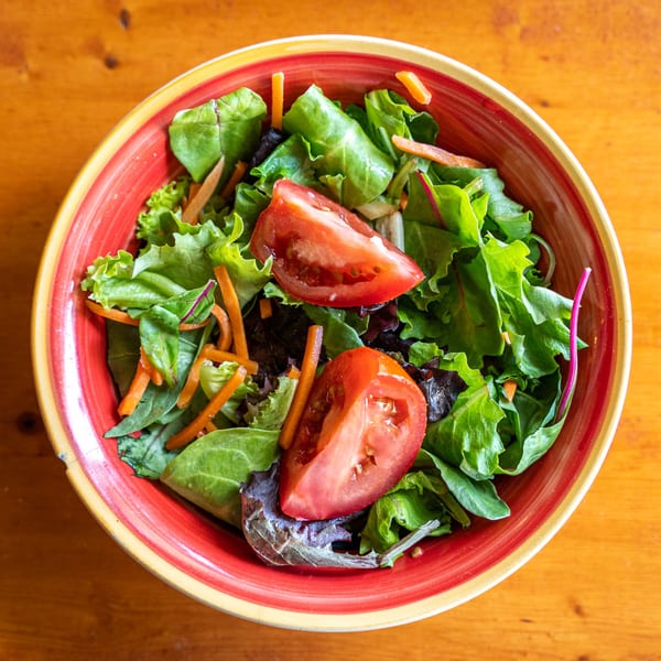 Fresh green salad with sliced tomatoes and shredded carrots in a vibrant red and yellow bowl.