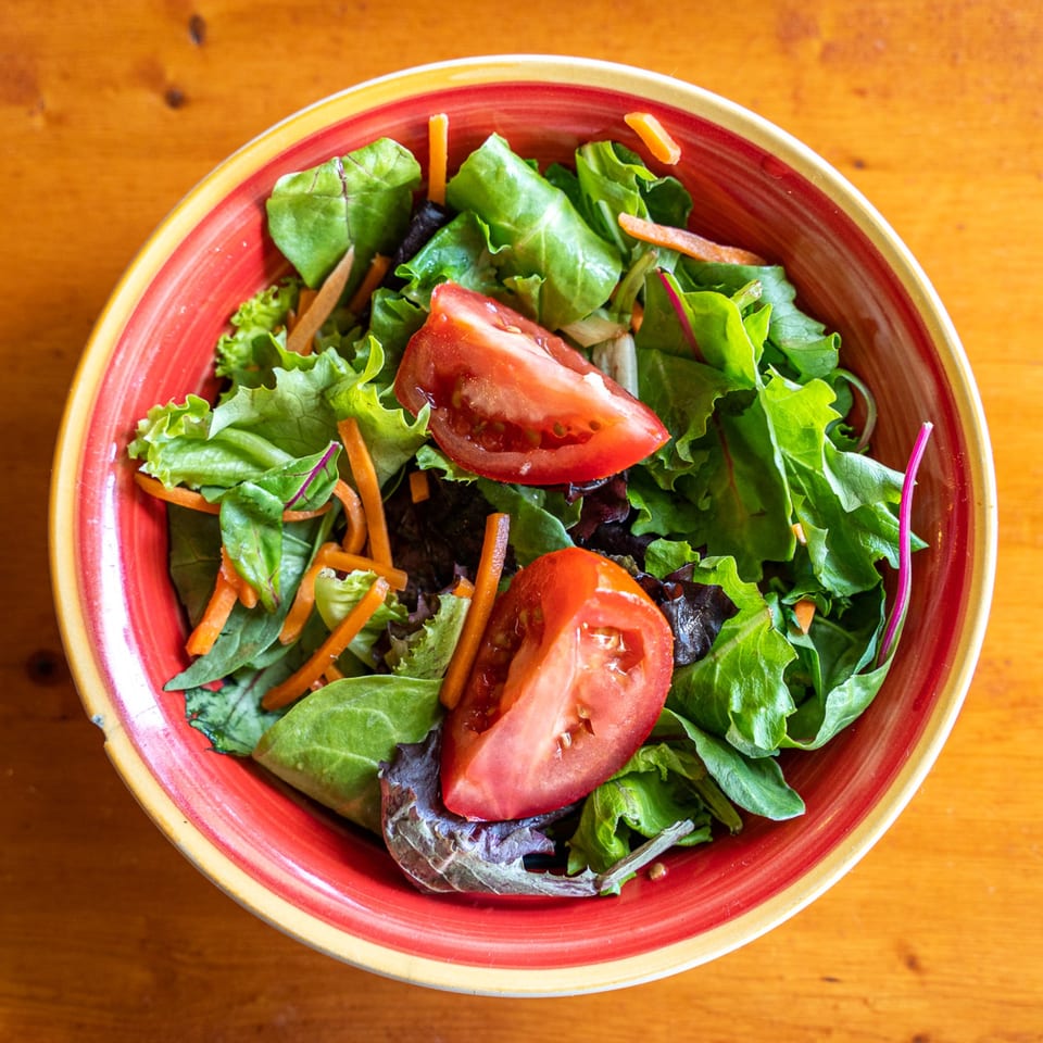Fresh green salad with sliced tomatoes and shredded carrots in a vibrant red and yellow bowl.