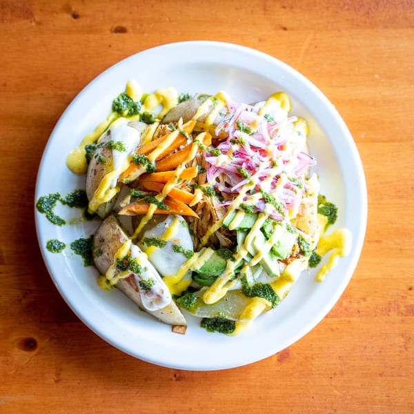 Peruvian dish with potatoes, shredded chicken, avocado, red onion, and various sauces on a white plate.