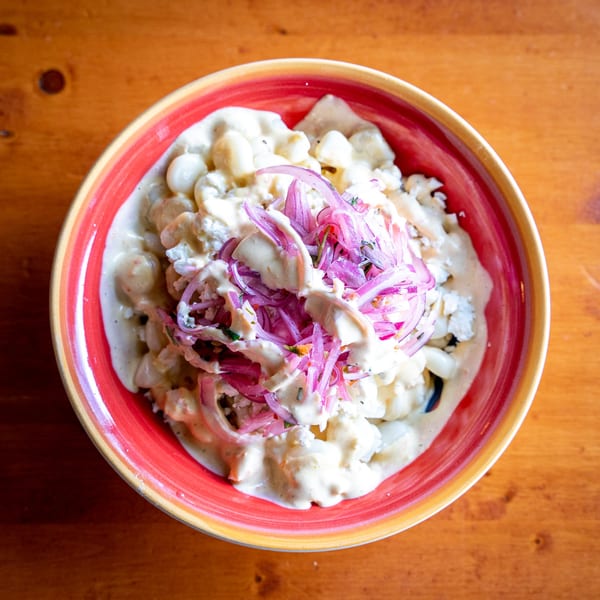 Overhead view of Peruvian corn salad with creamy dressing and red onions in a colorful bowl.