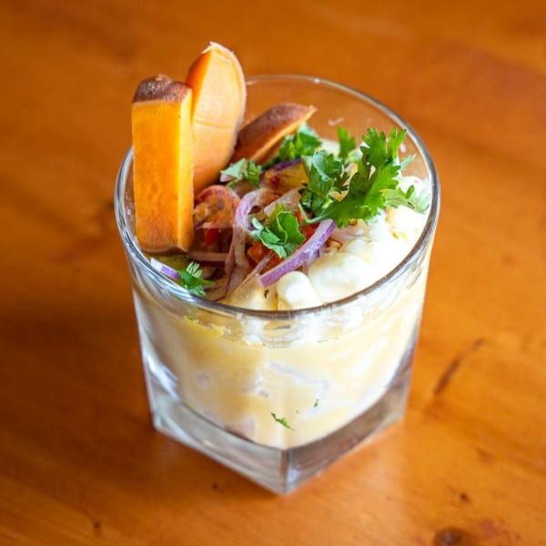 Peruvian ceviche in a glass, with sweet potato, corn, red onion, and cilantro on a wooden table.