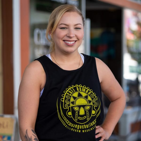 A smiling woman in a black Cafe Rumba tank top stands outside the restaurant.