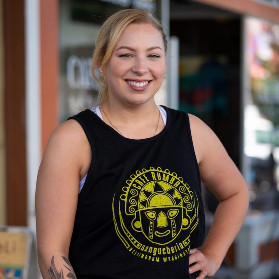 A smiling woman in a black Cafe Rumba tank top stands outside the restaurant.