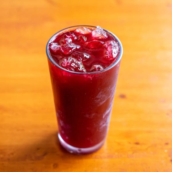 A tall glass of vibrant red Chicha Morada, a Peruvian drink, filled with ice on a wooden table.