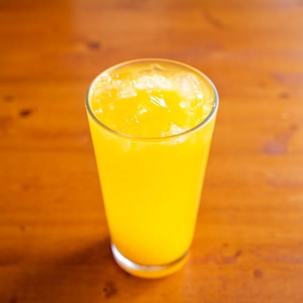 A tall glass of bright yellow Peruvian chicha morada with ice, on a wooden table.