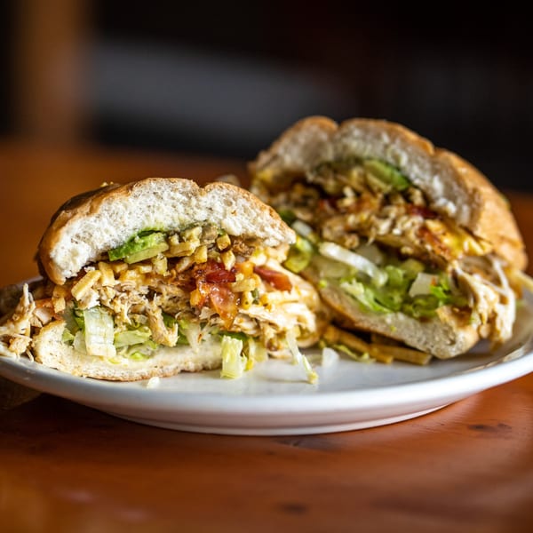Two halves of a Peruvian chicken sandwich with lettuce, avocado, and fries on a white plate.